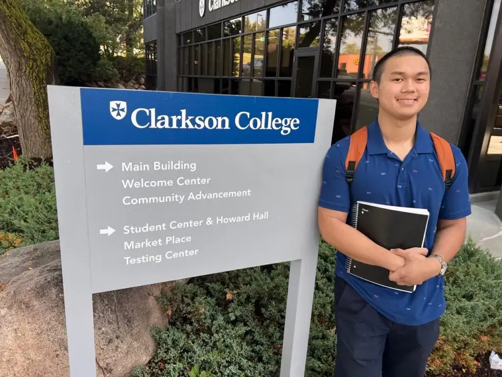 Jimmy Nguyen next to a sign for Clarkson College.